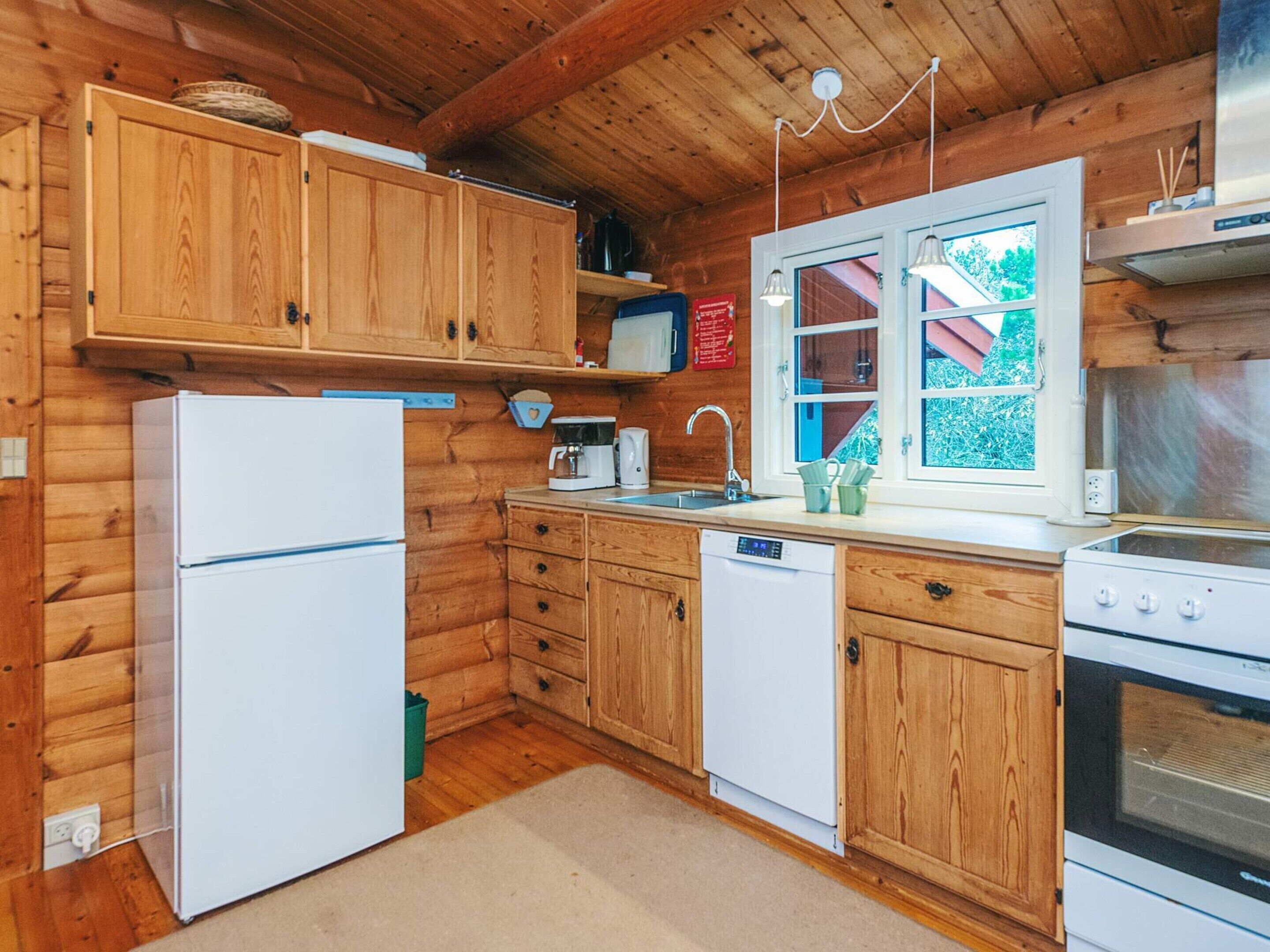 Cucina di una baita in legno con frigorifero, lavastoviglie, fornello e pensili in legno.