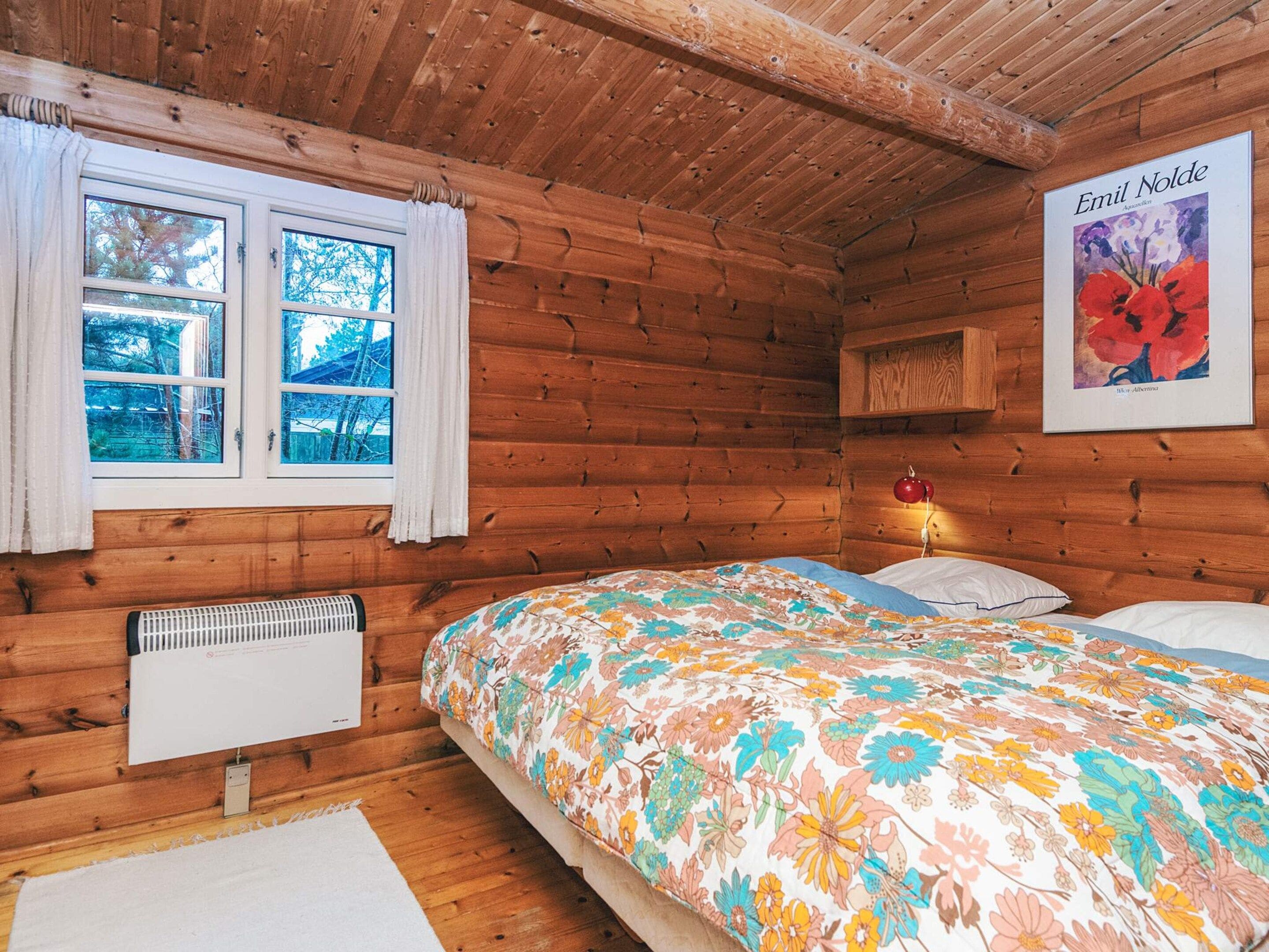 A wooden cabin room with a bed, a radiator, and a window with curtains.