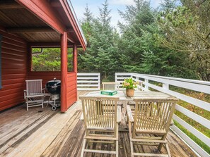 A wooden deck with a red building, a barbecue grill, and a table with chairs. - 6 Person Holiday Home in Oksbol (Oksbol)