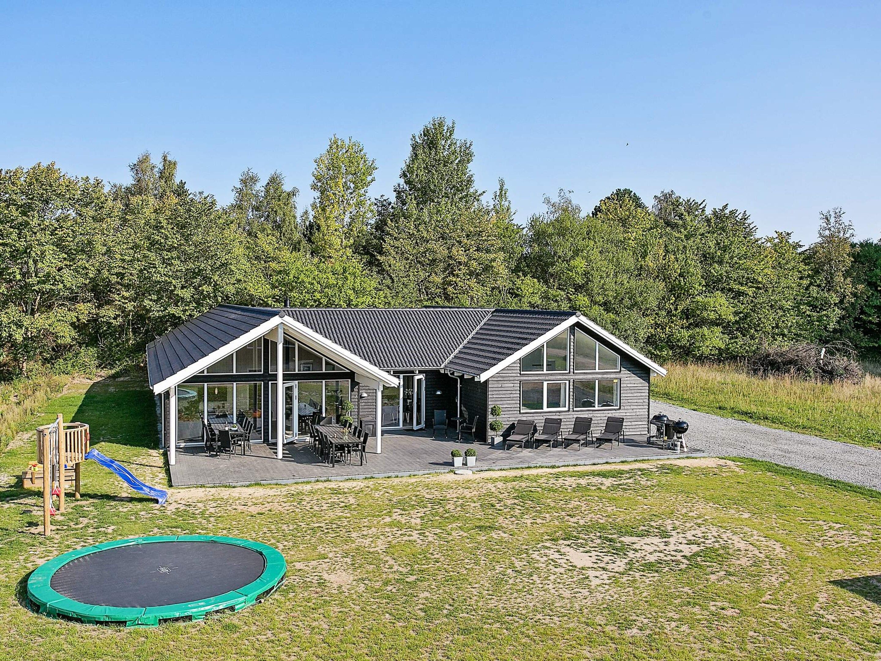 A modern house with a covered patio, a trampoline, and a wooden play structure.