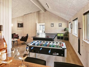 A room with wooden walls and ceiling, a foosball table, a dartboard, and a window with blinds.