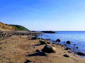 Una playa con costa rocosa, cielo despejado y una vista distante de un cerro verde.