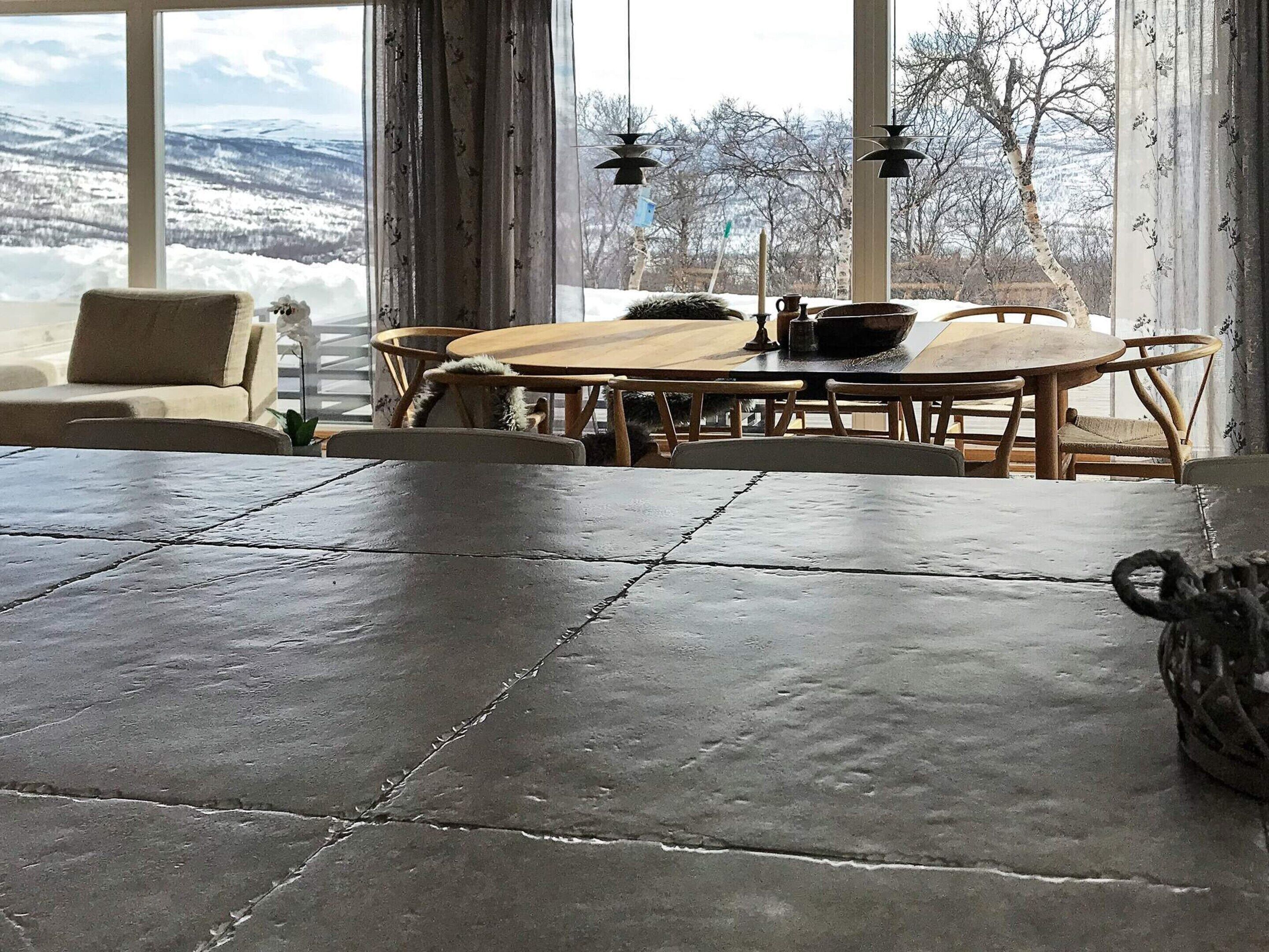 A dining area with a stone table and chairs, a wooden dining table, and a view of snow-covered mountains through large windows.