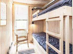 Ein Stockbett mit einer Matratze, ein Korbstuhl und ein Fenster mit Jalousien.