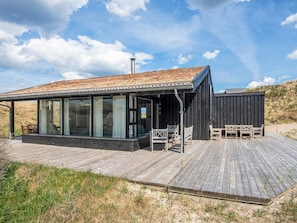 A modern building with large glass windows, a wooden deck, and outdoor seating. - 4 Star Holiday Home in Pandrup (Pandrup)