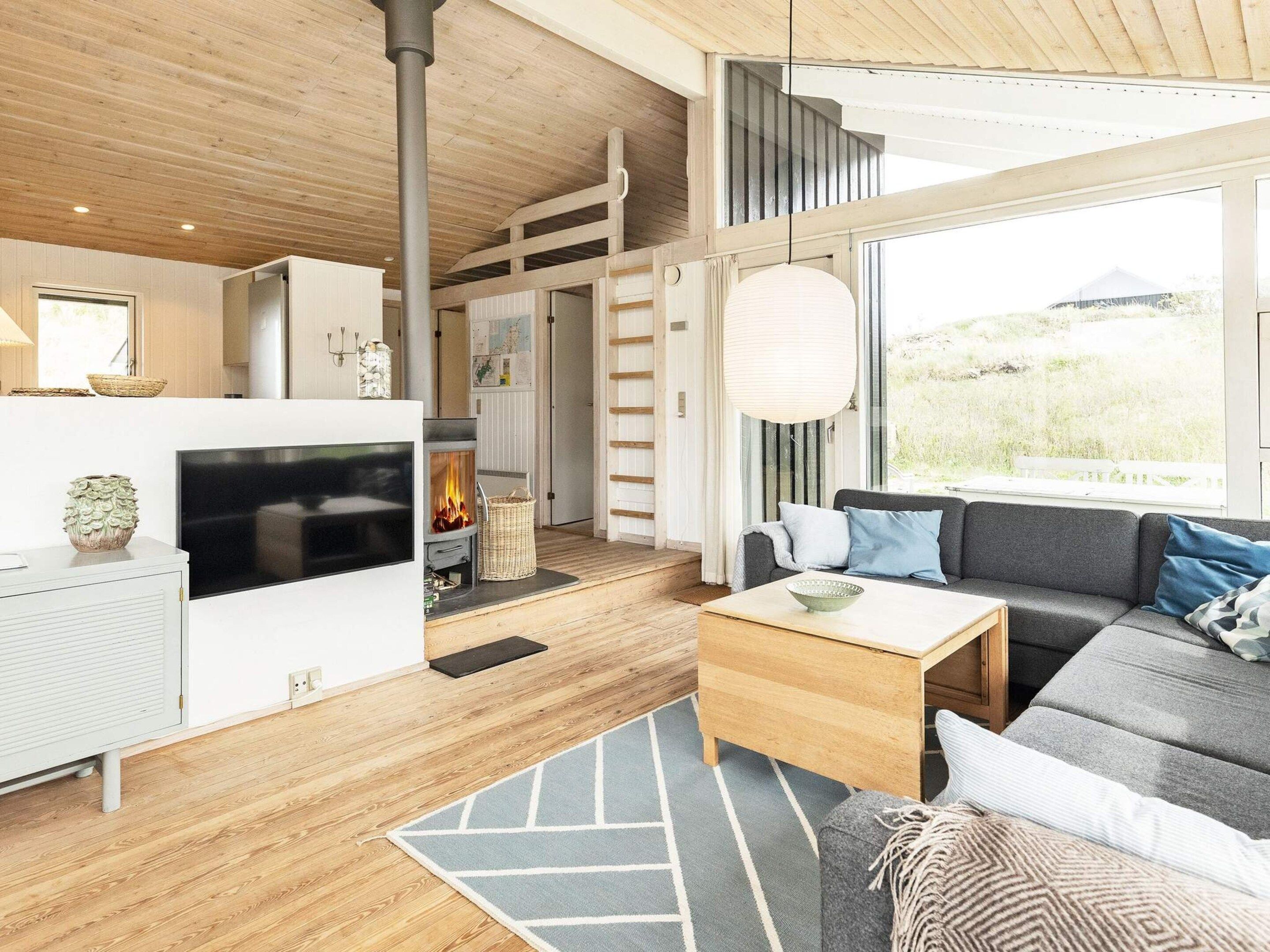 Una sala de estar moderna con chimenea, sofá y ventanas amplias.