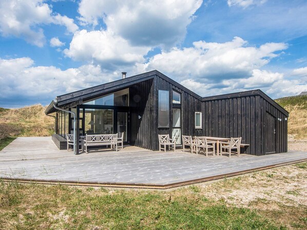 A modern black building with a glass entrance, wooden deck, and outdoor seating.