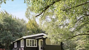 A log cabin with a stone foundation, a porch with wooden steps, and a view of a lush green garden. - 4 Person Holiday Home in Allinge (Allinge)