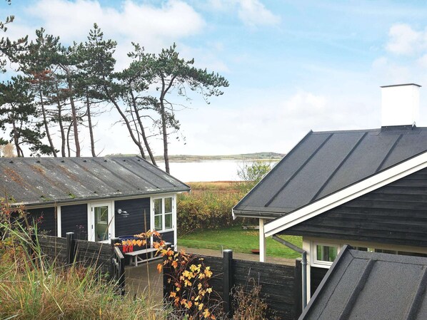 A rustic cabin with a metal roof, surrounded by a wooden deck and a fenced garden area. - 4 Person Holiday Home in Martofte-by Traum (Martofte)
