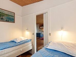 A bedroom with two beds, a painting on the wall, and a view into the kitchen area. - 4 Person Holiday Home in Martofte-by Traum (Martofte)