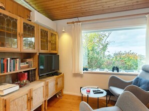 A cozy living room with a television, bookshelves, a window with a view of trees, and a seating area with a table. - 4 Person Holiday Home in Martofte-by Traum (Martofte)