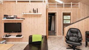 Um interior moderno com parede de madeira, TV de tela plana, sofá, poltrona de couro preto, escada e uma pequena prateleira com objetos decorativos.