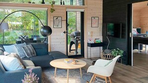 A modern living room with a sofa, a round coffee table, and a rocking chair. There is a door leading to another room with a grill and a TV. - 5 Star Holiday Home in Hals (Hals)