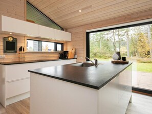 A modern kitchen with a large island, wooden cabinetry, and a view of the outdoors.