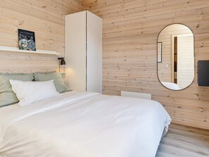 A bedroom with a bed, a wardrobe, a mirror, and a shelf with a book.
