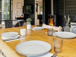 Una mesa de comedor dispuesta con platos, cubiertos y vasos, con una chimenea al fondo.