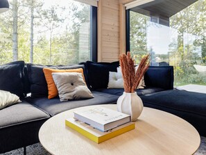 A modern living room with a dark-colored sofa, a round wooden coffee table, and a white vase with dried plants. - 5 Star Holiday Home in Hals (Hals)