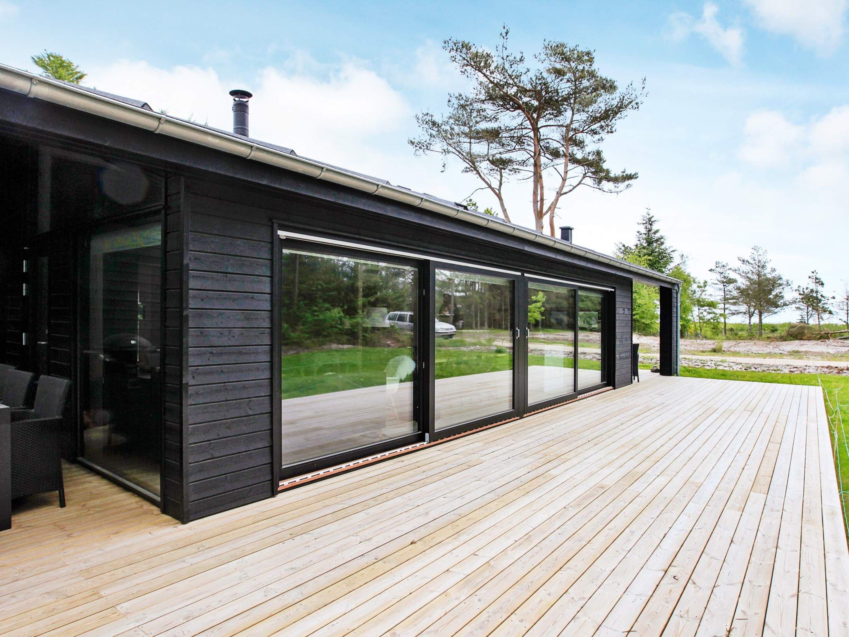 Una casa moderna con un gran ventanal corredero, una terraza de madera y vistas del paisaje circundante.