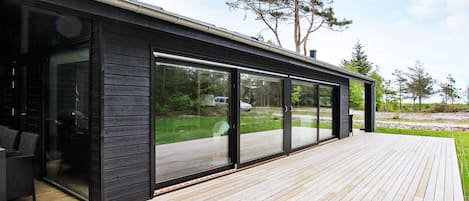 A modern house with a large sliding glass door, a wooden deck, and a view of the surrounding landscape.