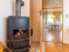 A room with a wood-burning stove, a dining area with a table and chairs, and a wooden ceiling.