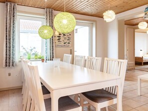A dining area with a white table and chairs, two hanging lamps, and a window with curtains.