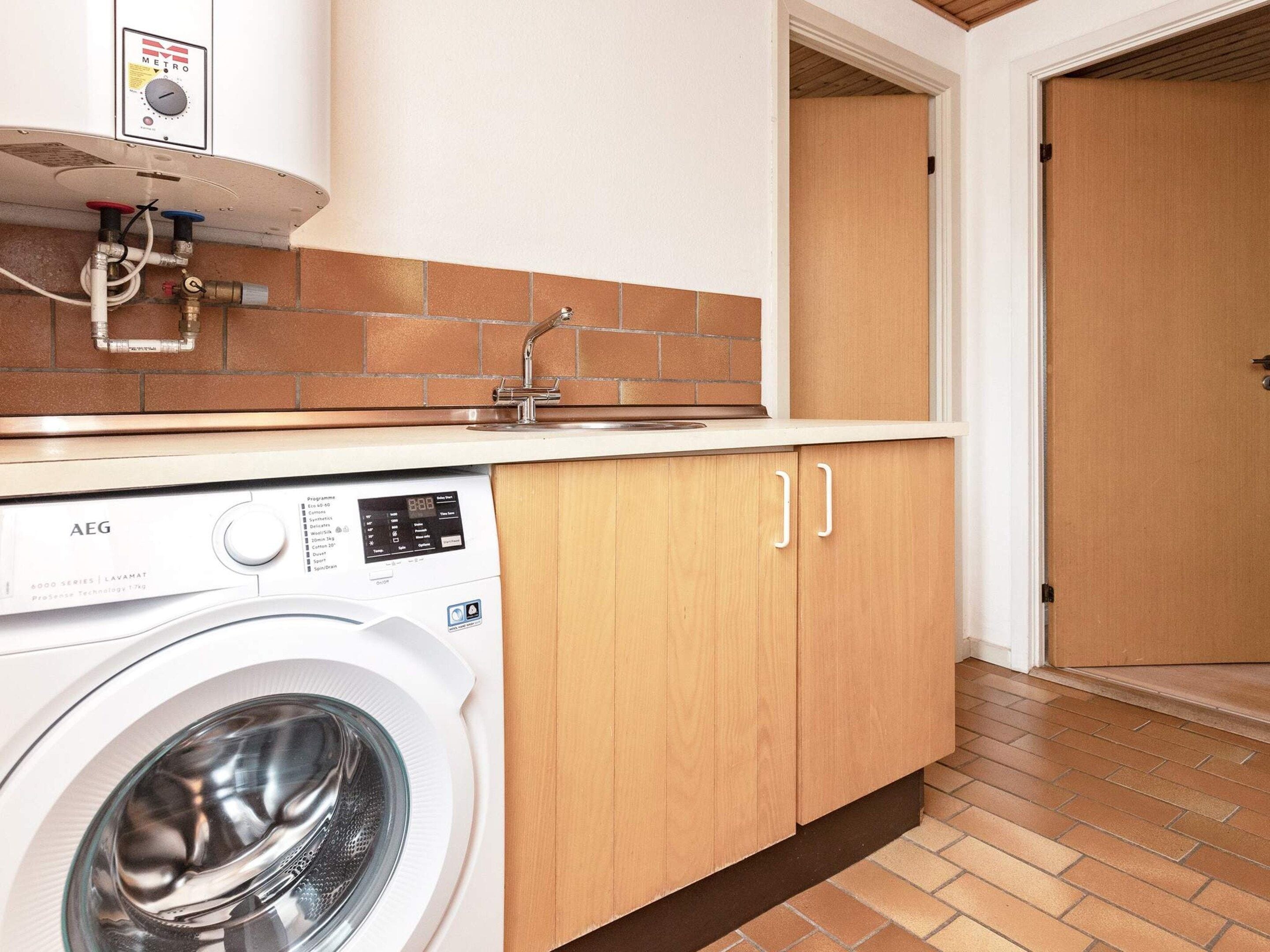 A compact kitchen with a washing machine, a sink, and a door leading to another room.