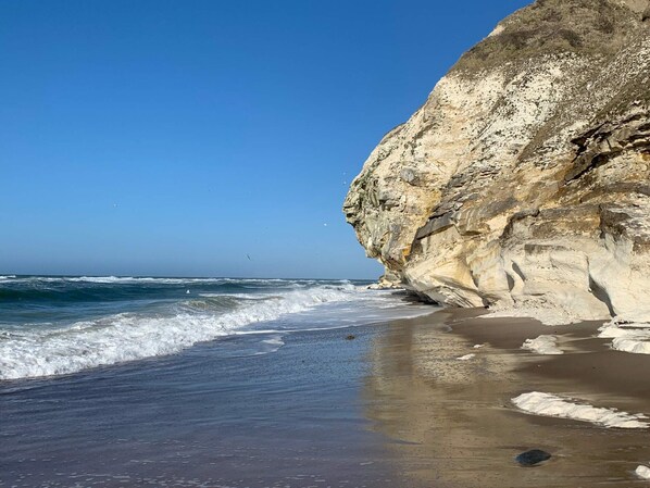 A coastal beach with a large rock formation and waves.