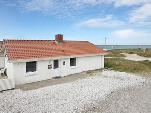 A single-story building with a red-tiled roof, a small porch, and a gravel driveway.