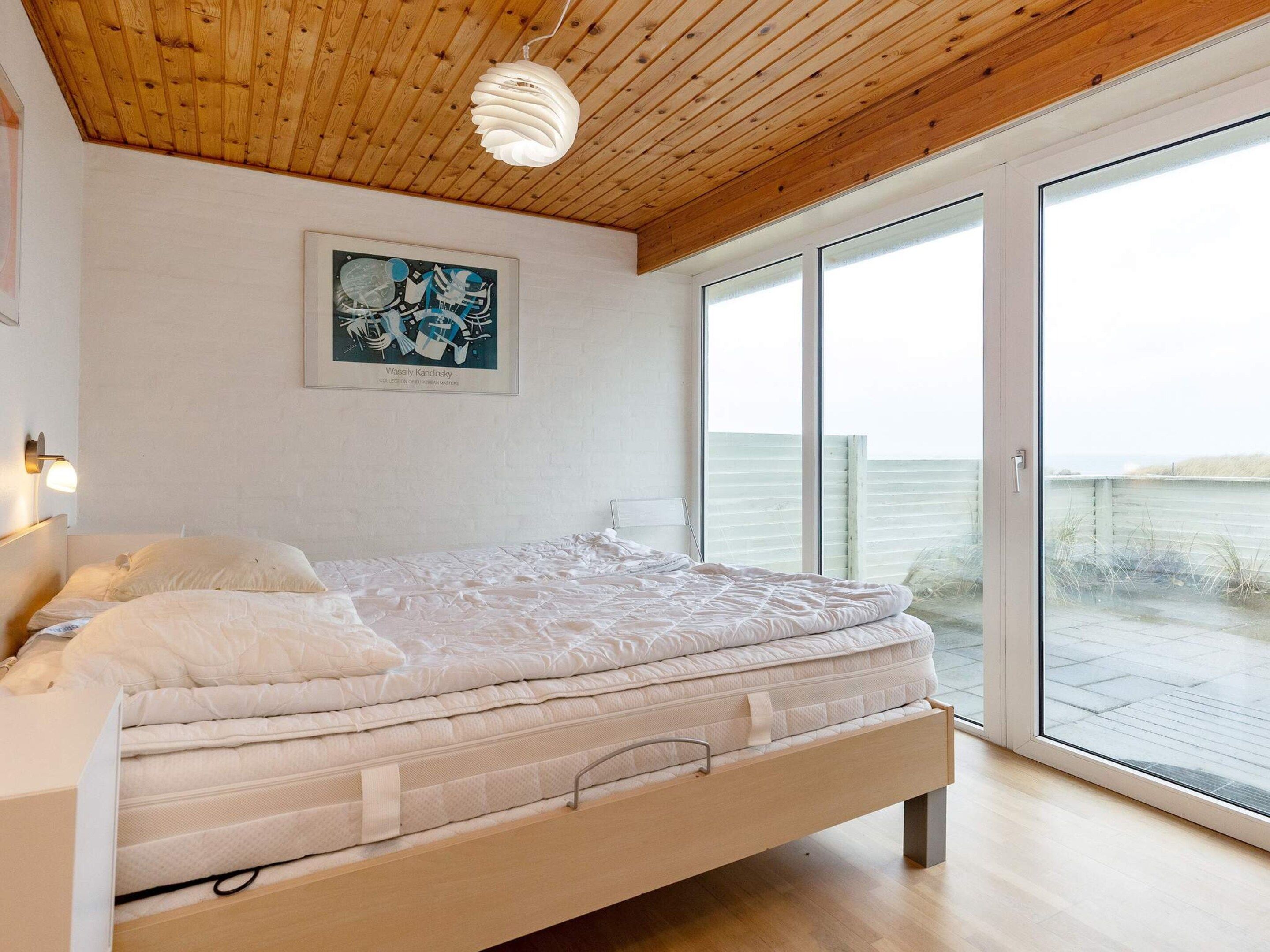 A bedroom with a bed, a ceiling light, a window, and a painting on the wall.