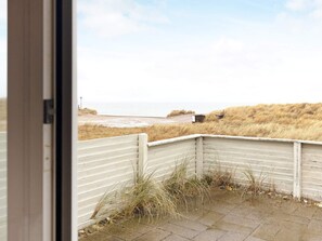 A view from a window overlooking a beach with a white fence and a small structure in the distance. - 8 Person Holiday Home in Frostrup (Frøstrup)