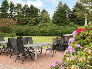 An outdoor patio with tables and chairs, surrounded by greenery and trees.