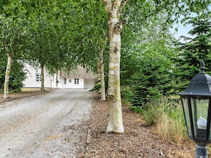A gravel driveway leading to a white building with a traditional design, surrounded by trees and a lamp post.