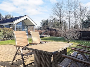 A patio with a table and chairs, a small garden, and a house in the background. - 5 Star Holiday Home in Hals (Hals)