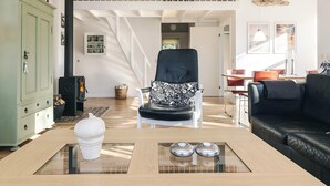 A spacious living room with a high ceiling, a black leather sofa, a white armchair with a patterned cushion, and a glass coffee table. - 5 Star Holiday Home in Hals (Hals)