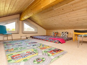 A room with a sloped ceiling, two beds with colorful bedding, a blue chair, a small table, and a window. - 5 Star Holiday Home in Hals (Hals)