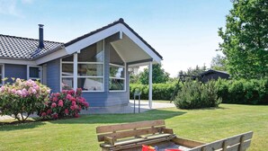 A house with a covered porch, a wooden play area with sand and buckets, and a lawn with flowering bushes. - 5 Star Holiday Home in Hals (Hals)