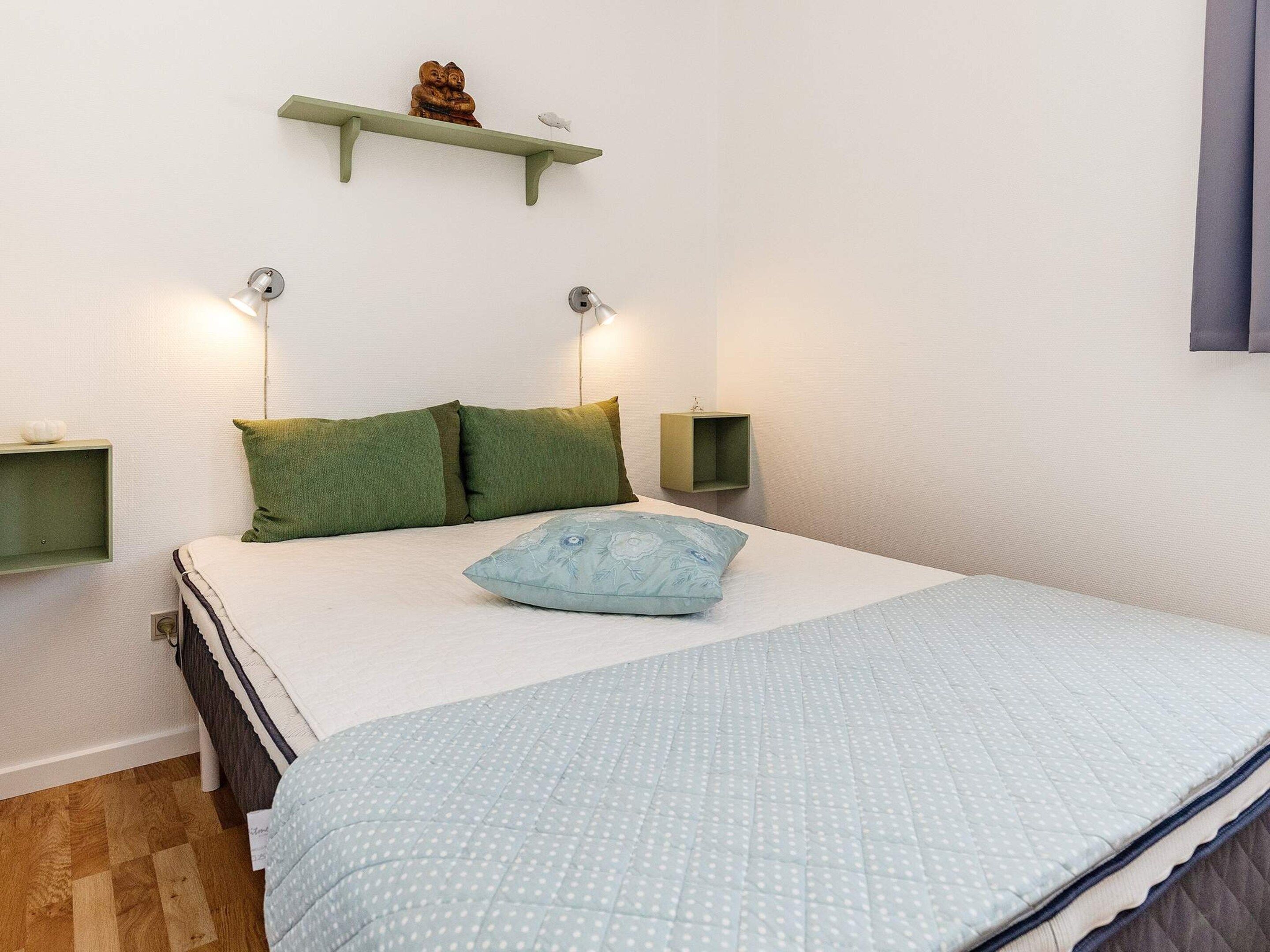 A bedroom with a bed, pillows, bedside tables, and wall-mounted shelves.