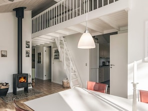 A modern interior with a central fireplace, a dining area, and a kitchen with a staircase leading to an upper level. - 5 Star Holiday Home in Hals (Hals)