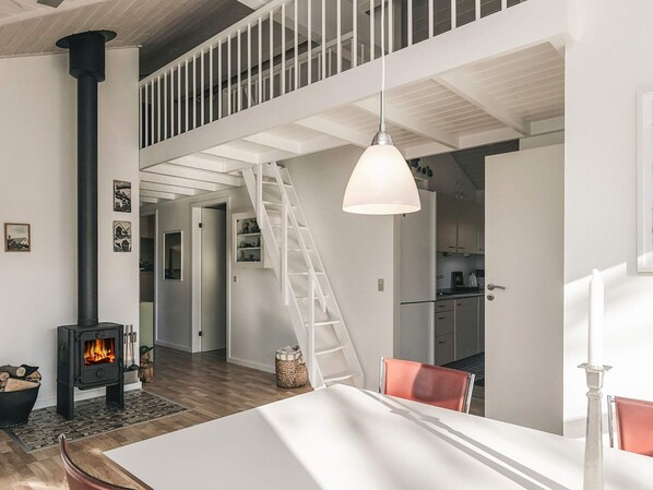 A modern interior with a central fireplace, a dining area, and a kitchen with a staircase leading to an upper level.