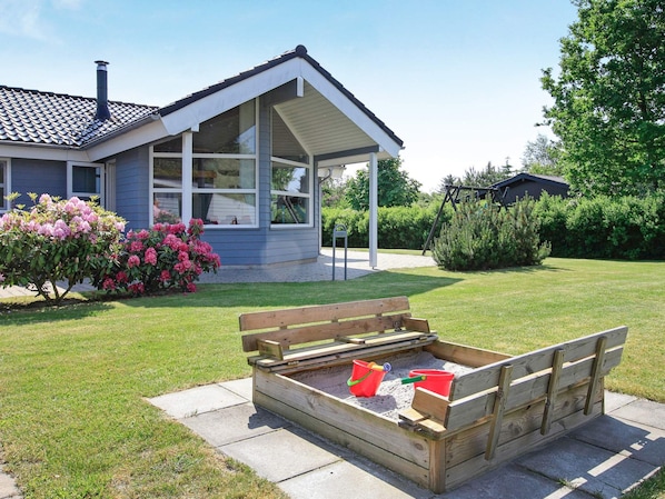 A house with a covered porch, a garden with flowering shrubs, and a wooden sandbox with two buckets. - 5 Star Holiday Home in Hals (Hals)