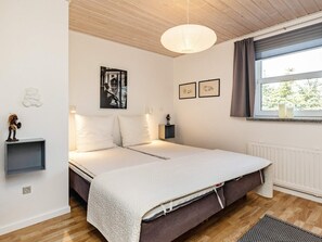 A bedroom with a bed, a bedside table, a lamp, a window with curtains, and artwork on the wall.