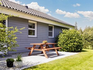 A house with a tiled roof, a wooden picnic table, and a garden with potted plants.