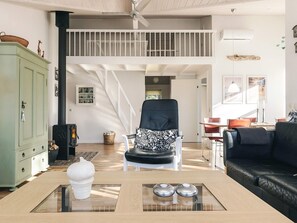 A spacious living area with a high ceiling, a staircase, a black leather sofa, a glass coffee table, and a green cabinet.