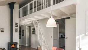 A modern interior with a central table, a staircase, a kitchen, and a visible chimney. - 5 Star Holiday Home in Hals (Hals)