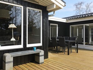 A deck with a table and chairs, a bench, and large windows.