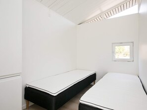 A small, white room with two single beds, a window, and a sloped ceiling.