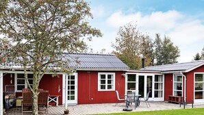 Punainen puutalo, jossa on katettu terassi, pieni puutarha ja yksi puu.