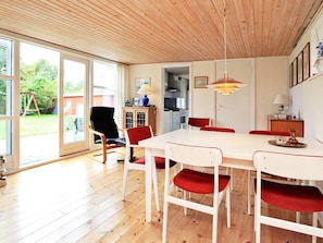 A dining area with a white table and red chairs, wooden flooring, a ceiling with wooden beams, and a view of the outdoors through glass doors. - 6 Person Holiday Home in Store Fuglede (Store Fuglede)