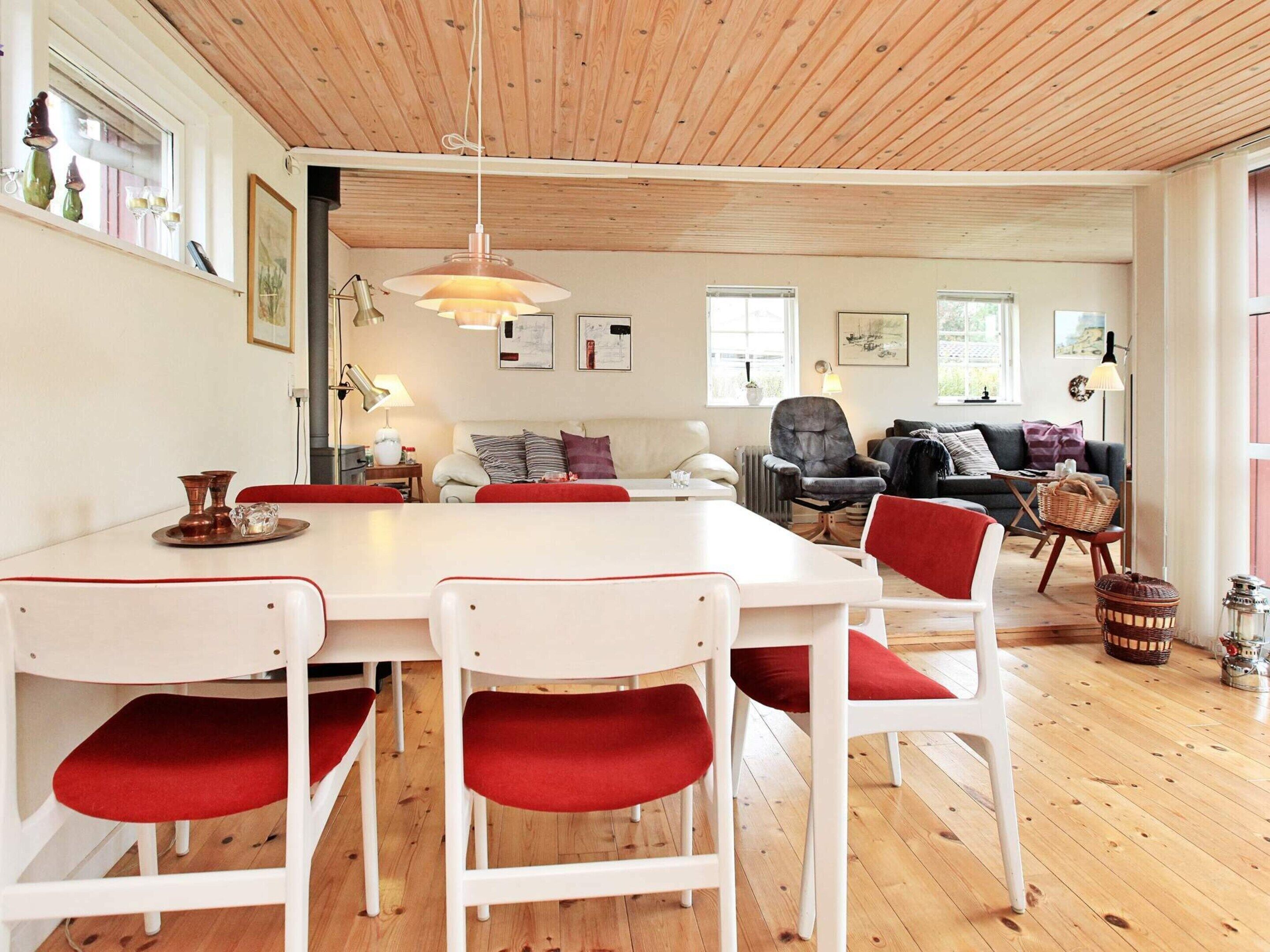 Un vaste espace de vie doté d’un plafond en bois, d’une table à manger avec des chaises blanches et d’un coin salon confortable avec un canapé et des fauteuils.