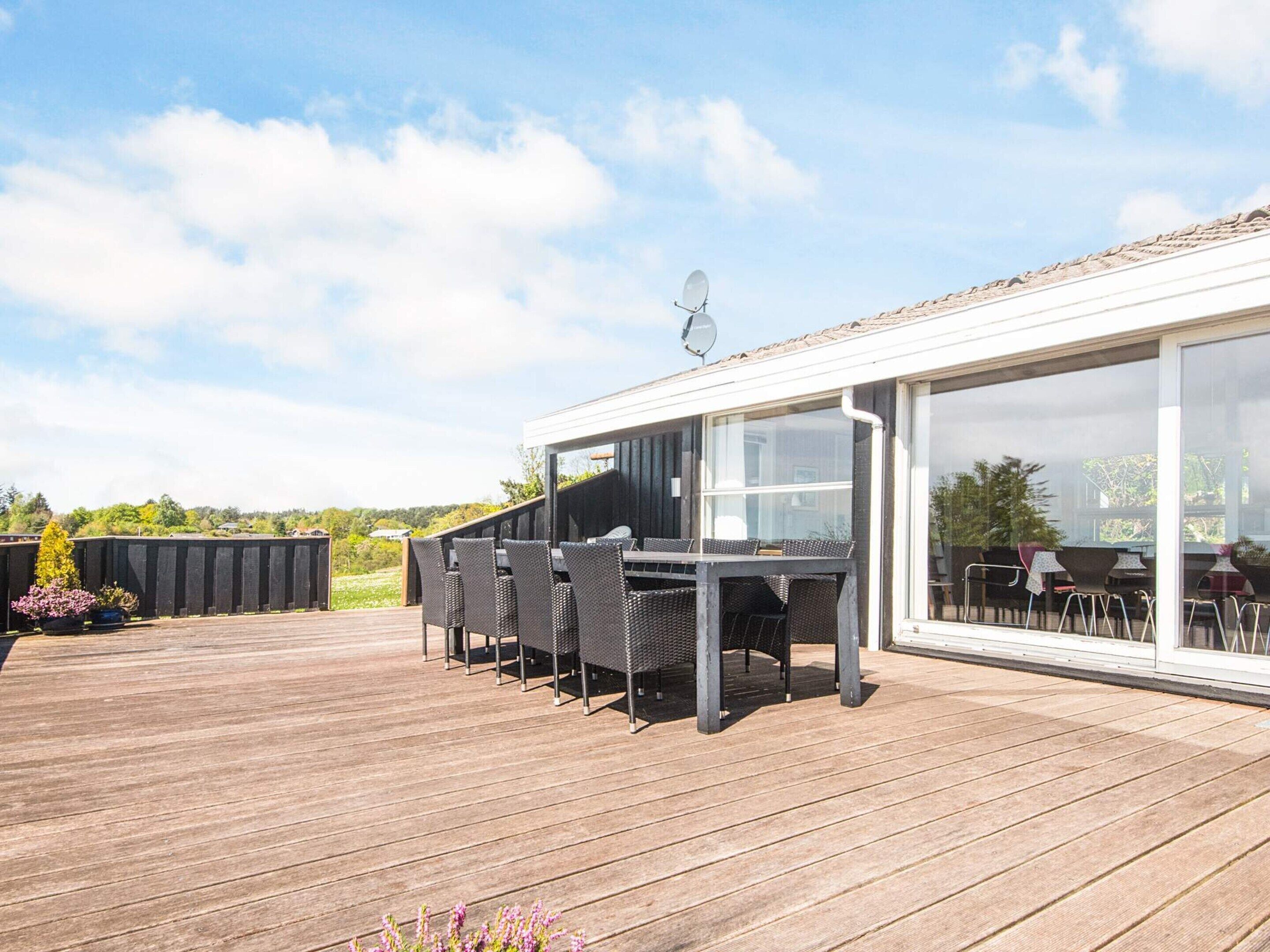 Una terraza exterior con zona de comedor, que incluye una mesa y sillas, y un salón con paredes de vidrio.